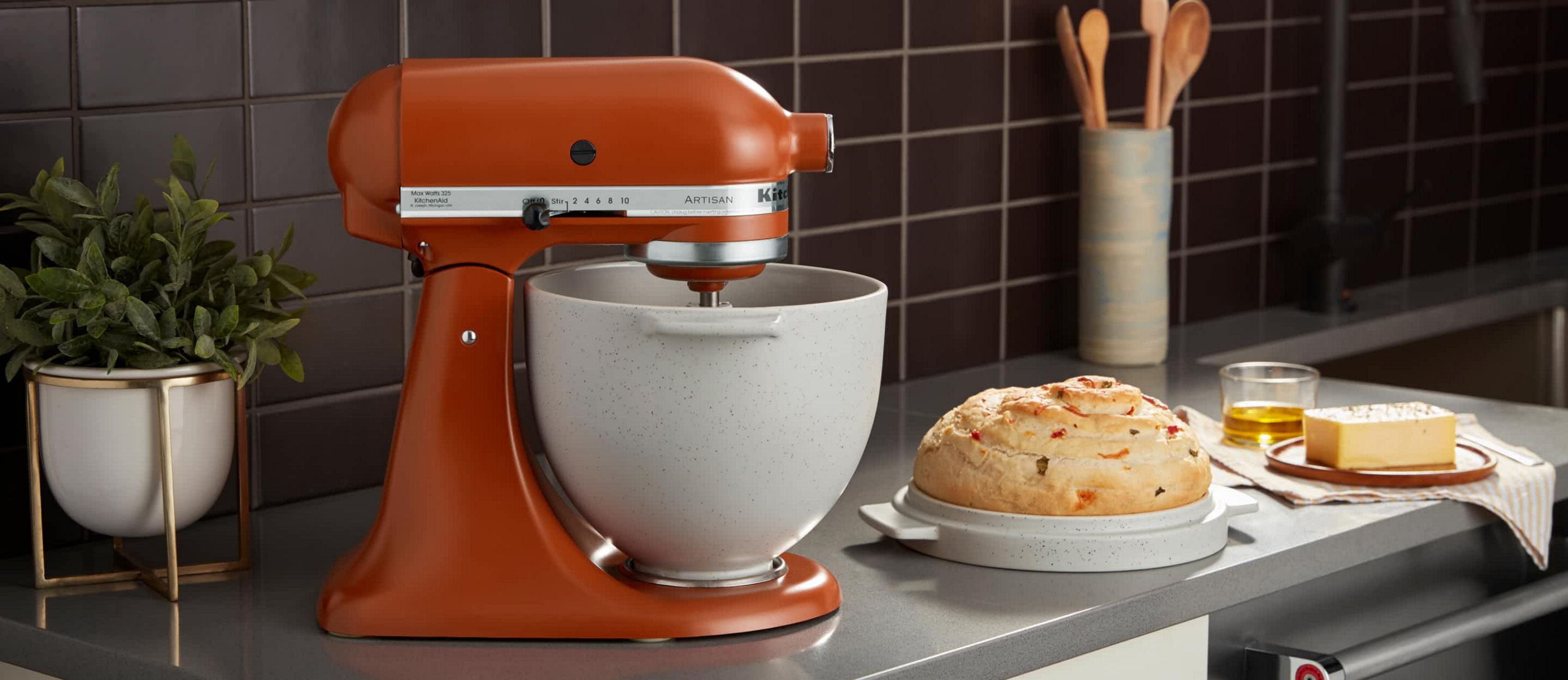 A KitchenAid® Stand Mixer using the Bread Bowl Attachment with a freshly baked loaf of bread in the Baking Lid. 