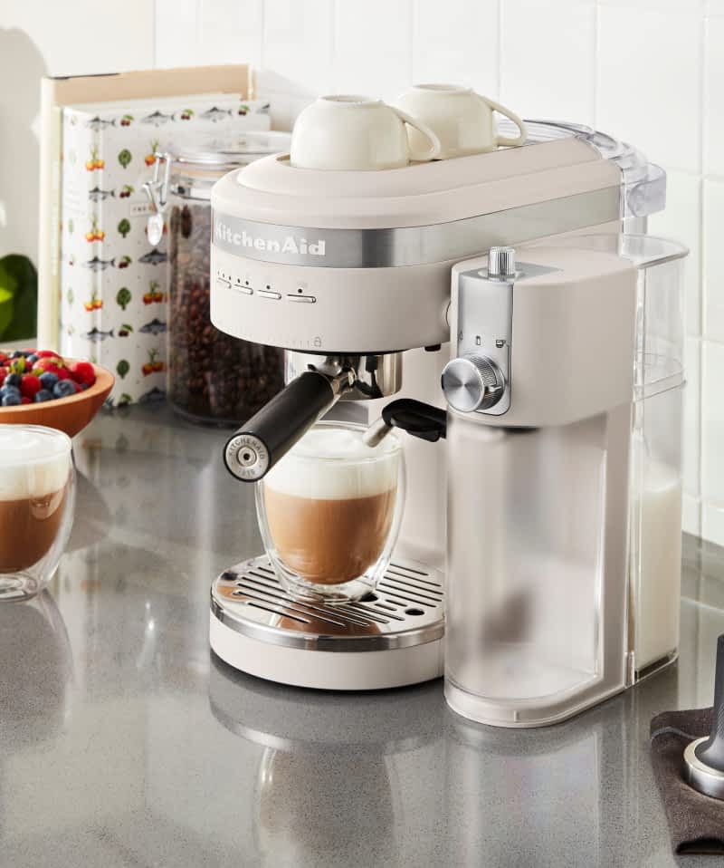 A KitchenAid® semi-automatic espresso machine with milk frother attachment brewing a latte. 