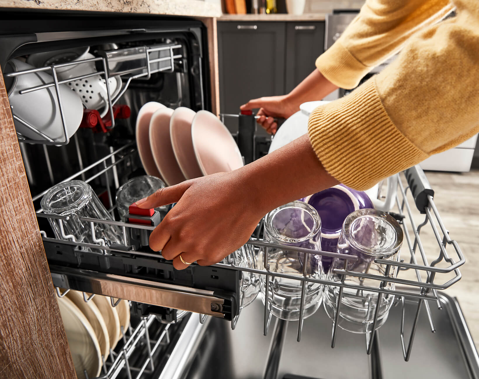 A person adjusting upper rack in a loaded dishwasher.